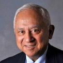 Older man smiling in formal attire against a grey background.