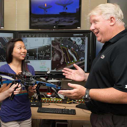 Two people discussing in front of a robotic device. image link to story