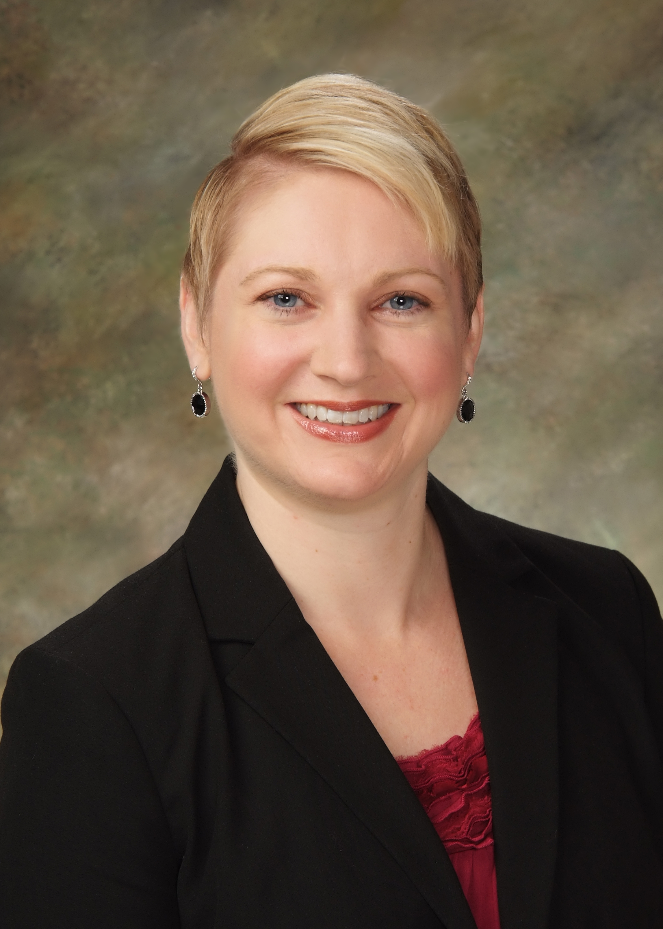 Woman in a black blazer with a neutral background.